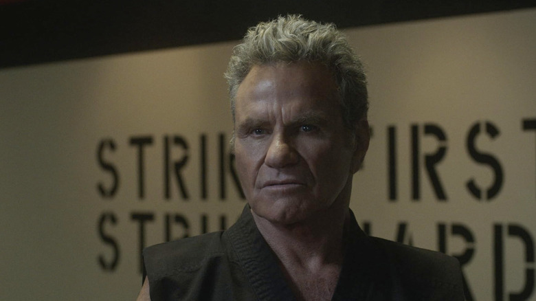 John Kreese standing in empty Cobra Kai dojo scowling
