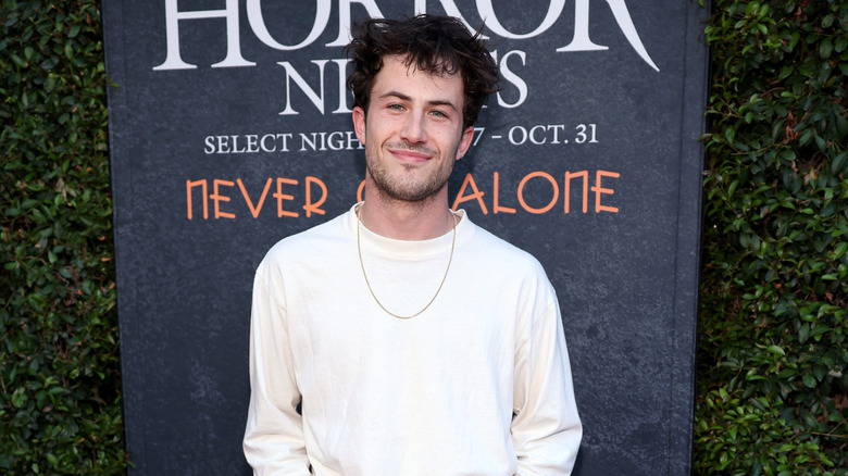 Dylan Minnette wearing a white shirt in front of a "Horror Nights" banner