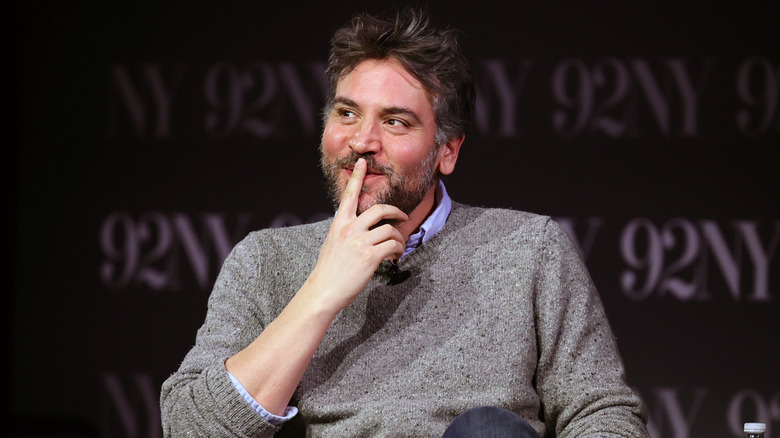 Josh Radnor smiling with a finger over his mouth