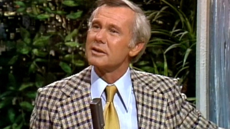 Johnny Carson sits at his desk and looks toward the left in The Tonight Show Starring Johnny Carson