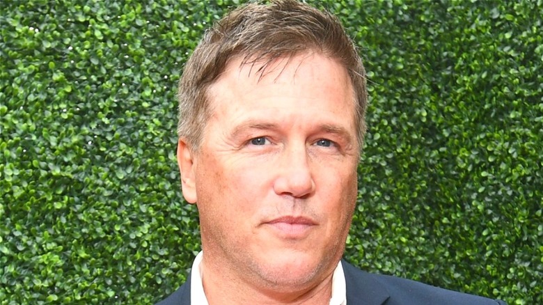 Lochlyn Munro smiles in front of a green backdrop