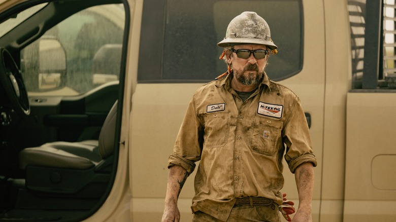 James Jordan as Dale on Landman, dirty in his work gear in front of an open pickup truck