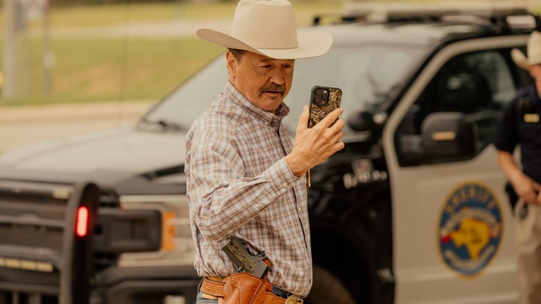 Mark Collie as Sheriff Walt, looking at his phone, in Landman