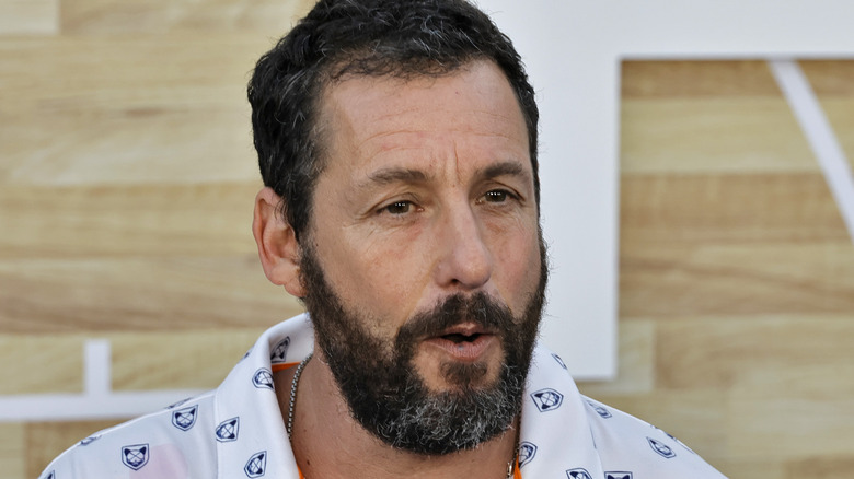 Adam Sandler with a greying beard and white shirt