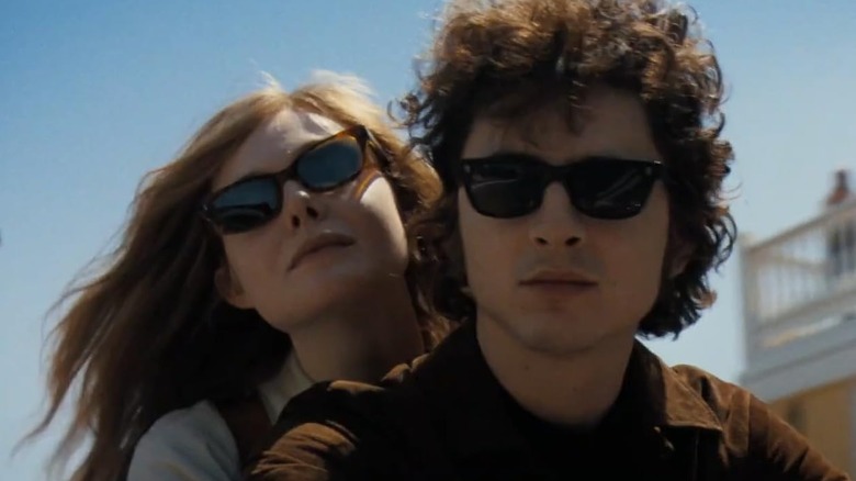 Sylvie riding with Bob on a motorcycle both of them wearing sunglasses in A Complete Unknown