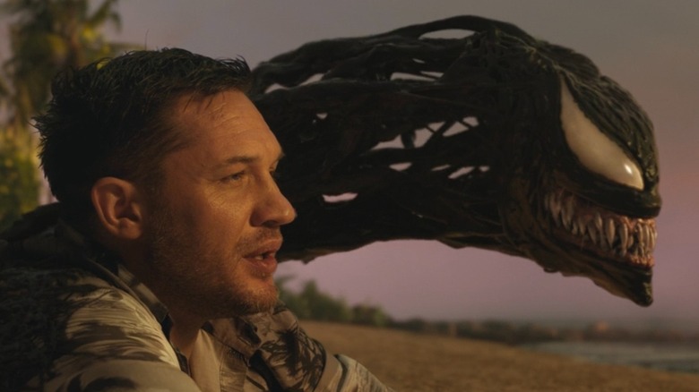 Eddie Brock sitting next to Venom on a beach in "Venom: Let There Be Carnage" (2021)