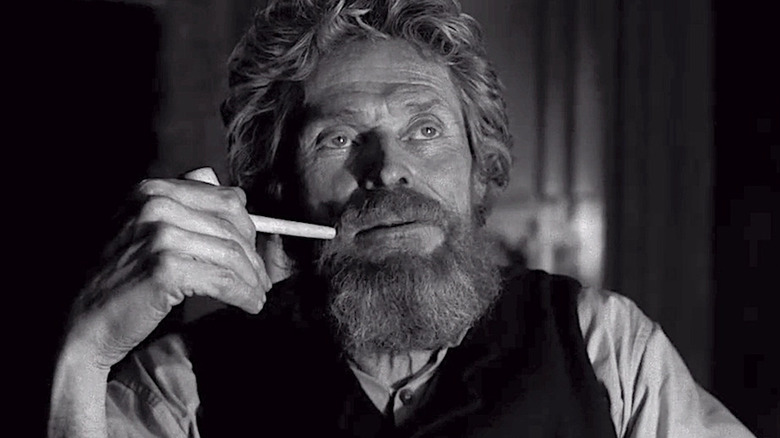 Willem Dafoe sits with a pipe