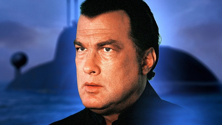 Steven Seagal, face slightly bloated, set in front of a submarine