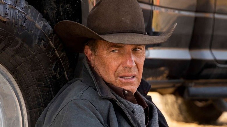 John Dutton sitting on the ground against a truck in 