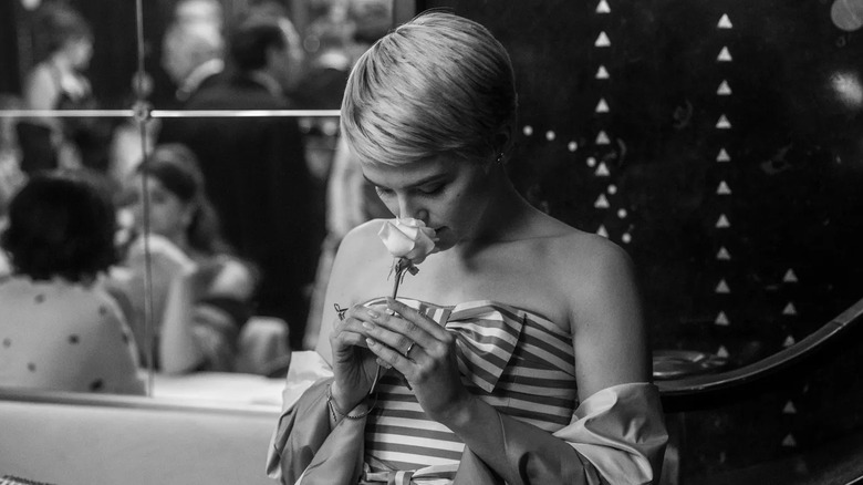 Jean in a gown in front of a mirror smelling a rose in Nouvelle Vague